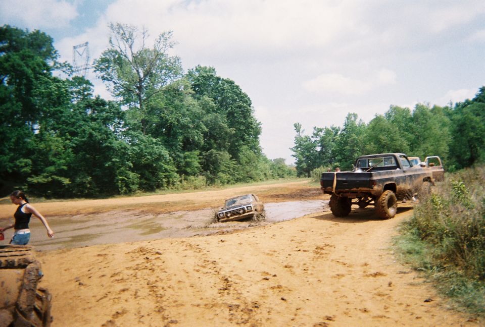 Muddy trucks stuck in a dirt track with trees and a cloudy sky