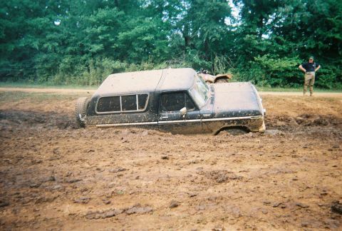 1978 Ford Bronco - A black 1978 Ford Bronco is deeply stuck in mud, with a person standing in the background.