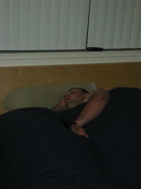 1992 Ford Crown Victoria - A man sleeps soundly in bed, covered by a dark blue blanket, with blinds visible in the background.
