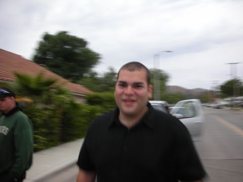 1992 Ford Crown Victoria - A man in a black polo shirt smiles while walking down a sidewalk with another person and vehicles in the background.