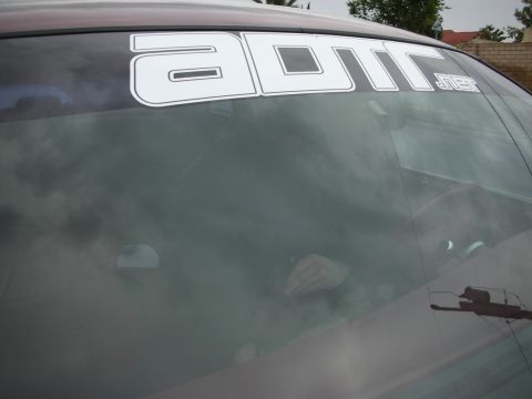 1992 Ford Crown Victoria - A white banner with dark outlines is affixed to the top of the windshield of a dark-colored vehicle.