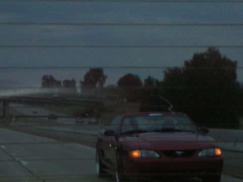 1992 Ford Crown Victoria - Red convertible driving on highway at dusk with trees and overpass in background.
