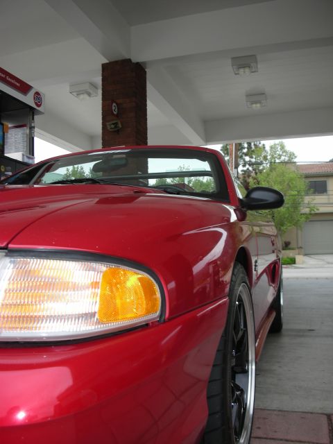 1992 Ford Crown Victoria - A red 1994 Ford Mustang convertible is parked at a gas station, showing its front quarter panel and wheel.