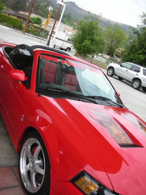 1992 Ford Crown Victoria - A red convertible sports car with a "True Forged" banner on the windshield is parked near a silver SUV.