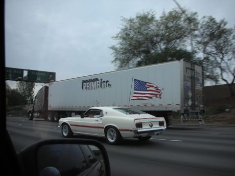 1992 Ford Crown Victoria - A white 1969 Ford Mustang Mach 1 with a red stripe drives on the highway next to a Prime Inc. semi-trailer truck.