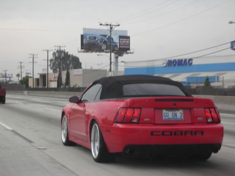 1992 Ford Crown Victoria - A red convertible sports car drives on the highway, displaying 'COBRA' on its rear.