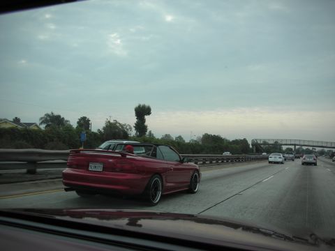 1992 Ford Crown Victoria - A red convertible Mustang drives down a highway under a cloudy sky.