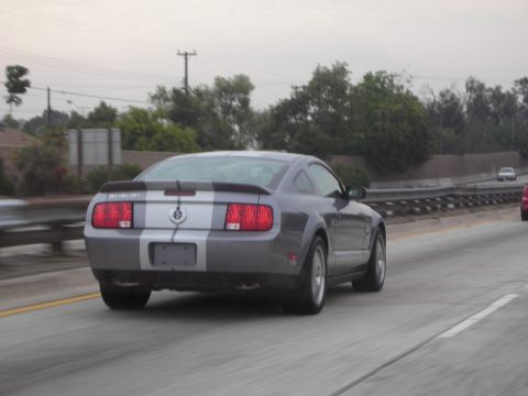 1992 Ford Crown Victoria - A gray Ford Mustang Shelby GT500 with racing stripes drives down a highway.