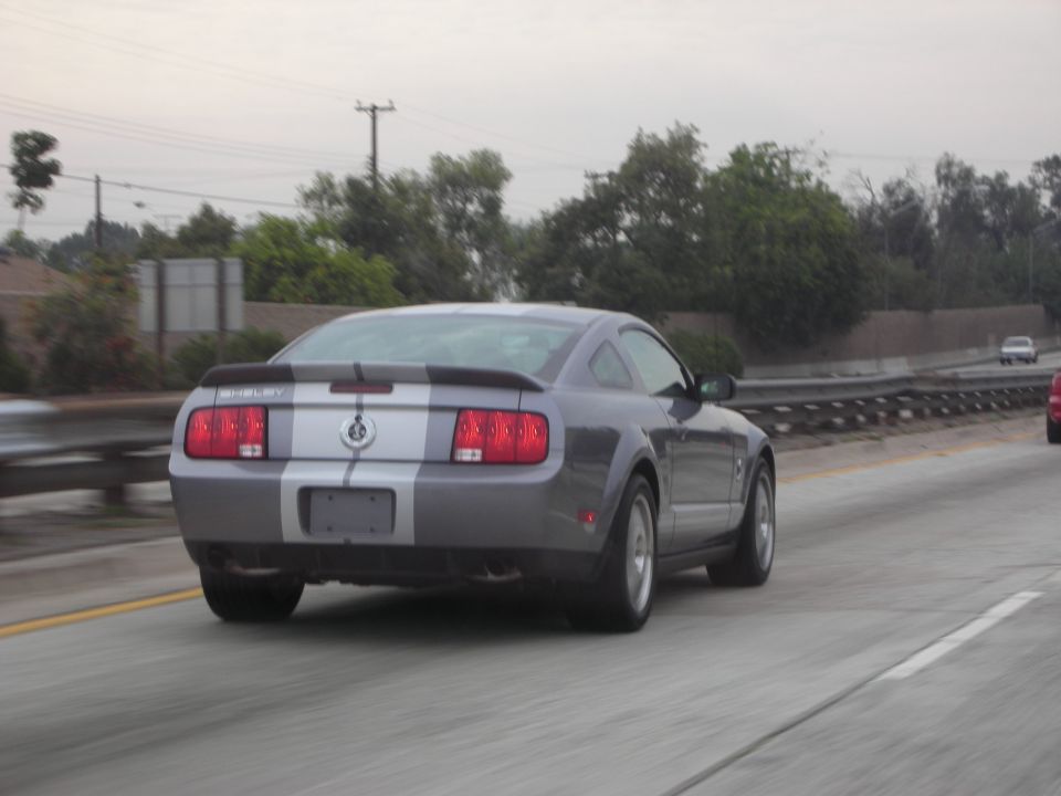 Gray Ford Mustang Shelby GT500 with silver racing stripes on rear, driving on highway