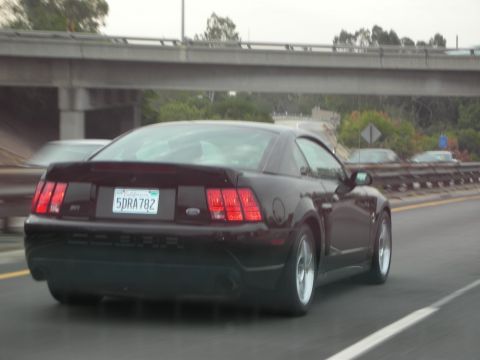 1992 Ford Crown Victoria - Rear view of a dark red 2000 Ford Mustang coupe driving on a highway.