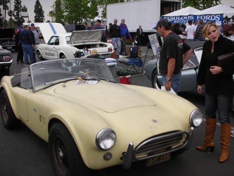 1992 Ford Crown Victoria - Yellow AC Cobra replica at a car show with other vehicles and people in the background.