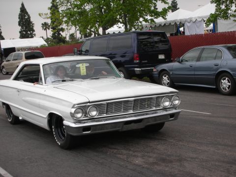 1992 Ford Crown Victoria - A white 1964 Ford Galaxie 500 coupe is seen from the front-right, with a blue van and sedan in the background.