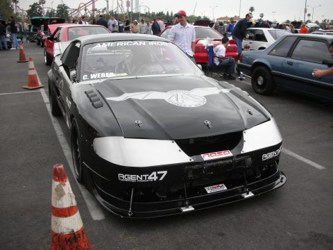 1992 Ford Crown Victoria - A black race car with prominent racing decals and silver accents is parked at an outdoor event.