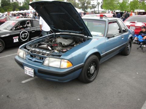 1992 Ford Crown Victoria - Blue police car with hood open at a car show, other vehicles and people in background.