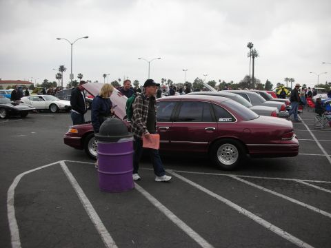 1992 Ford Crown Victoria - A maroon 1992 Ford Crown Victoria is parked at a car show, with people milling around and other vehicles visible.