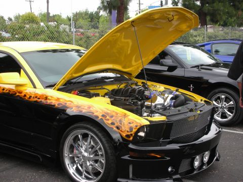 1992 Ford Crown Victoria - Modified Ford Mustang with flame graphics and custom wheels, hood open at a car show.