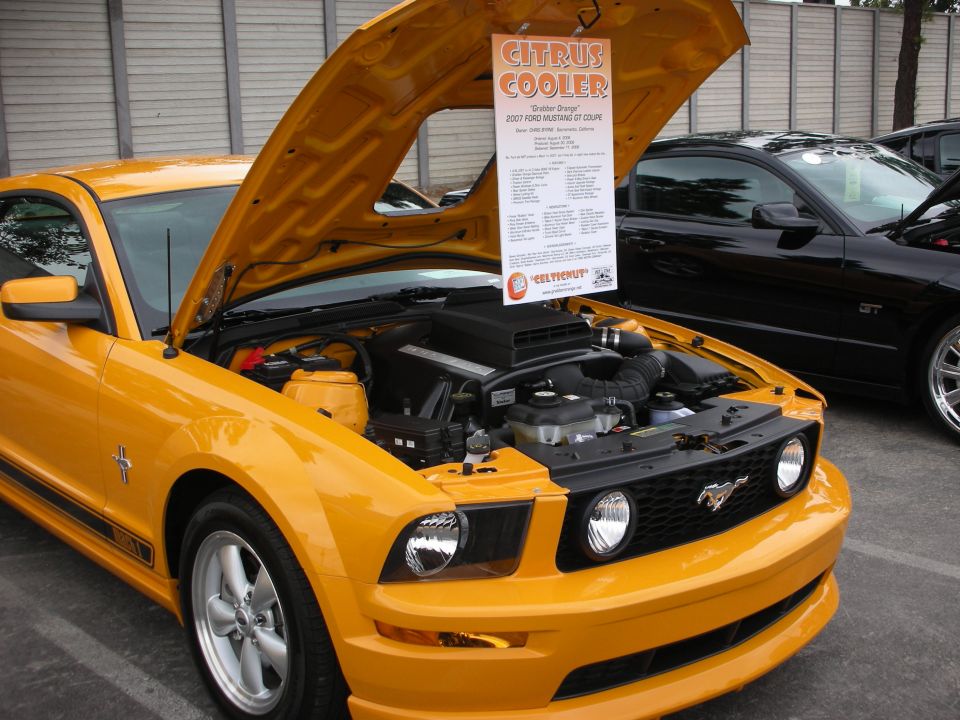 Yellow 2007 Ford Mustang GT coupe with hood open, showing engine. Black Ford Mustang GT in background