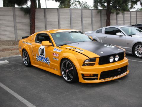 1992 Ford Crown Victoria - A yellow Ford Mustang with a black hood and racing decals is parked next to a silver car.