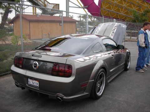 1992 Ford Crown Victoria - Gray Ford Mustang coupe with flame decals and hood open, parked at an outdoor event.
