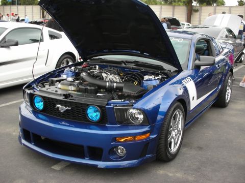 1992 Ford Crown Victoria - A blue Ford Mustang with its hood open is parked next to a white car at an outdoor car show.