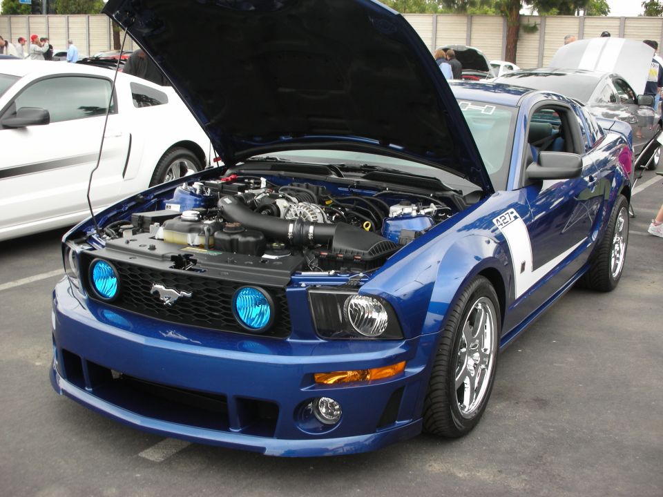 Blue Ford Mustang with hood open, showing engine and chrome wheels. "427" decal on fender