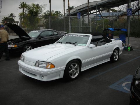 1992 Ford Crown Victoria - A white convertible Mustang is parked next to a black Mustang with its hood open.