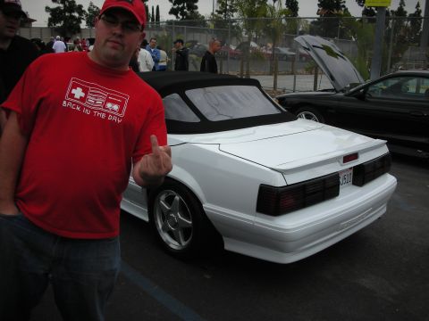1992 Ford Crown Victoria - A white convertible is parked next to a black car with its hood up.