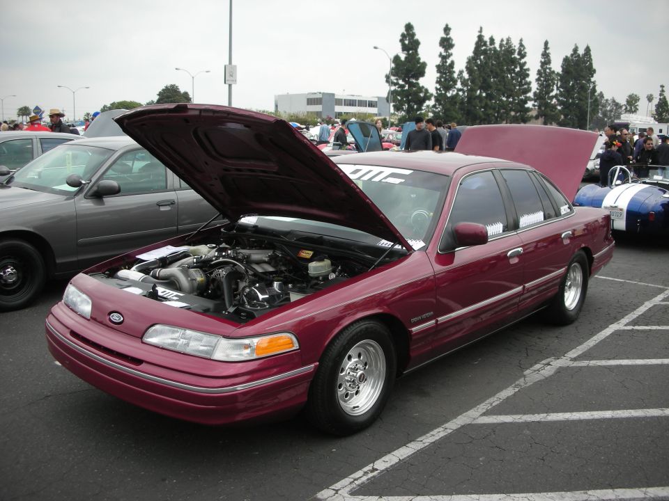 Maroon 1992 Ford Crown Victoria with hood open, showing engine modifications. Another Crown Victoria is parked to the left