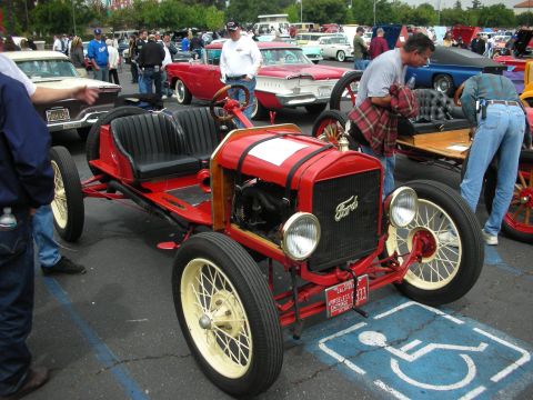 1992 Ford Crown Victoria - A vintage red Ford Model T is parked in a handicapped spot at a car show with other vehicles in the background.