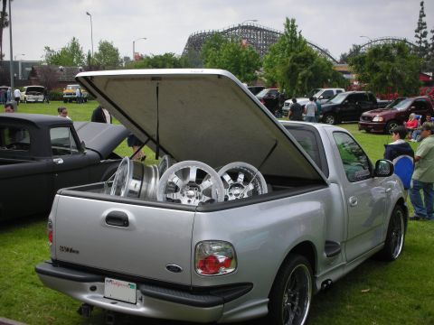1992 Ford Crown Victoria - A silver pickup truck is parked on grass with its bed cover open, revealing chrome wheels.