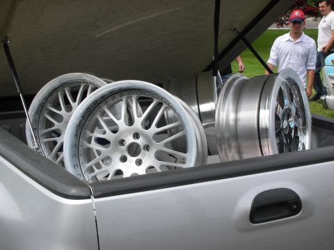 1992 Ford Crown Victoria - Several custom alloy wheels are transported in the bed of a silver pickup truck, with people visible in the background.