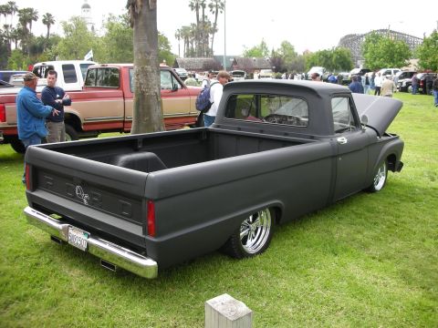 1992 Ford Crown Victoria - A matte black 1957 Ford pickup truck is parked on grass at an outdoor car show.