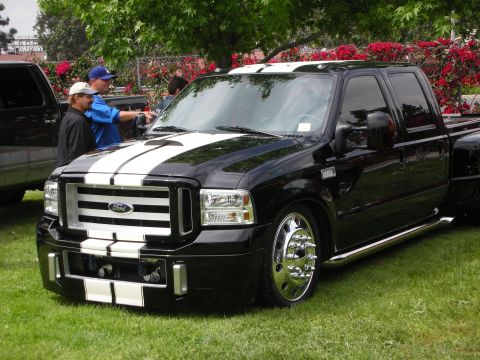 1992 Ford Crown Victoria - A black Ford Super Duty pickup truck with white racing stripes is parked on a grassy lawn with people nearby.