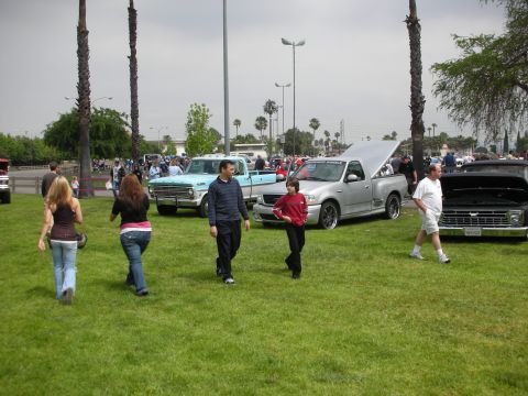 1992 Ford Crown Victoria - A gathering of vehicles and people on a grassy field under a cloudy sky.