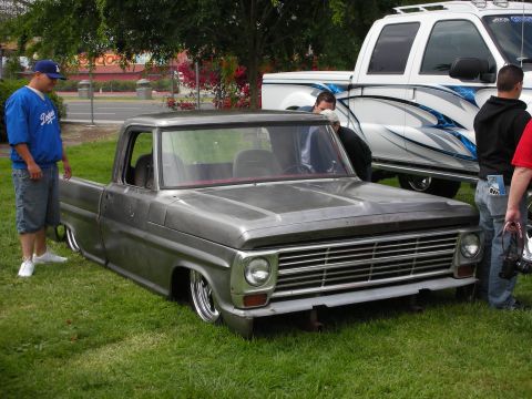 1992 Ford Crown Victoria - A custom gray pickup truck with a prominent chrome grille and a significantly lowered suspension sits on display next to a white truck.