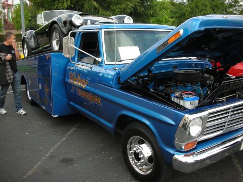 1992 Ford Crown Victoria - A blue tow truck is loaded with a black sports car, and a man is standing next to it.