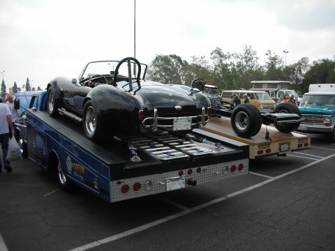 1992 Ford Crown Victoria - A black convertible sports car is transported on a tow truck, with another vehicle chassis on a trailer behind it.