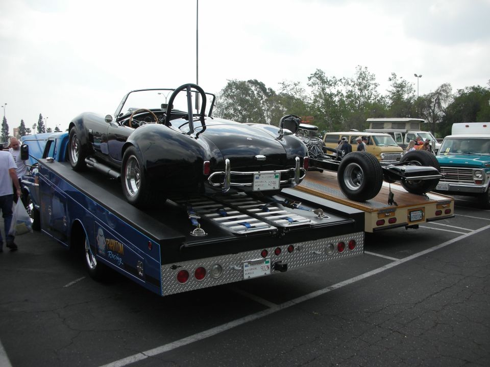 Black convertible sports car on a tow truck, rear view. Another car chassis on a trailer behind