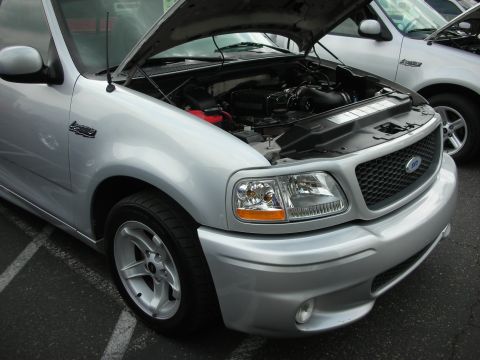 1992 Ford Crown Victoria - A silver 1999 Ford F-150 SVT Lightning pickup truck is parked with its hood open, revealing the engine compartment.