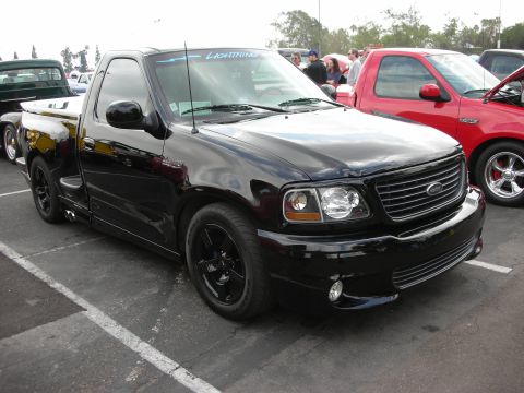 1992 Ford Crown Victoria - A black 1999 Ford F-150 Lightning pickup truck is parked at a car show next to a red truck.