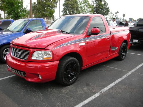 1992 Ford Crown Victoria - A red 1999 Ford F-150 SVT Lightning pickup truck is parked in a lot next to a blue truck.