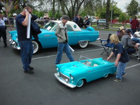 1992 Ford Crown Victoria - A man talks on his phone next to a classic turquoise Ford Thunderbird, while a child interacts with a smaller replica.