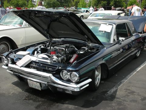1992 Ford Crown Victoria - A classic black Ford Thunderbird is displayed with its hood open, revealing a polished engine bay.