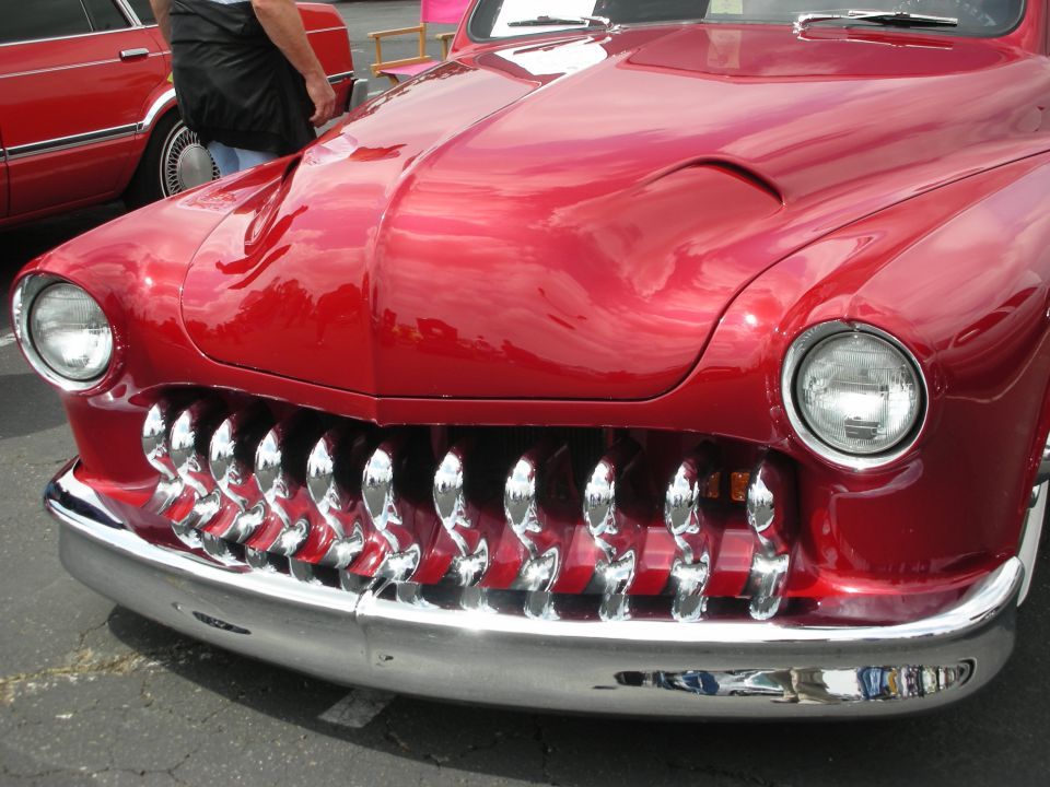 Red hot rod with a chrome grille many vertical teeth and a scooped hood
