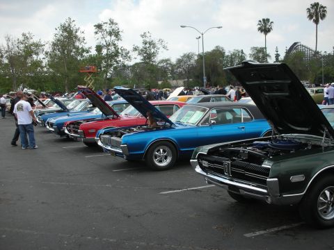 1992 Ford Crown Victoria - A car show features multiple classic vehicles with their hoods open, parked in rows under a cloudy sky.