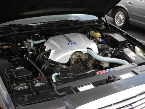 1992 Ford Crown Victoria - The engine bay of a dark blue car is shown, with a silver engine cover and blue stripes, alongside another vehicle in the background.