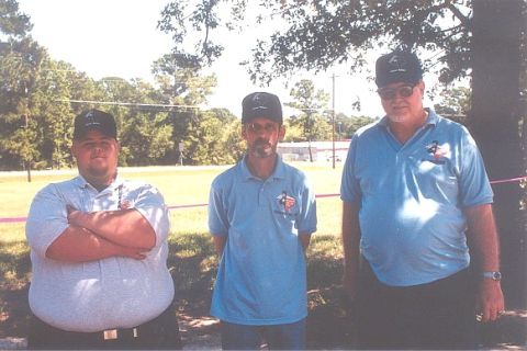 2002 Ford Crown Victoria - Three men are standing outside in front of trees and a field. The man on the right wears a watch.