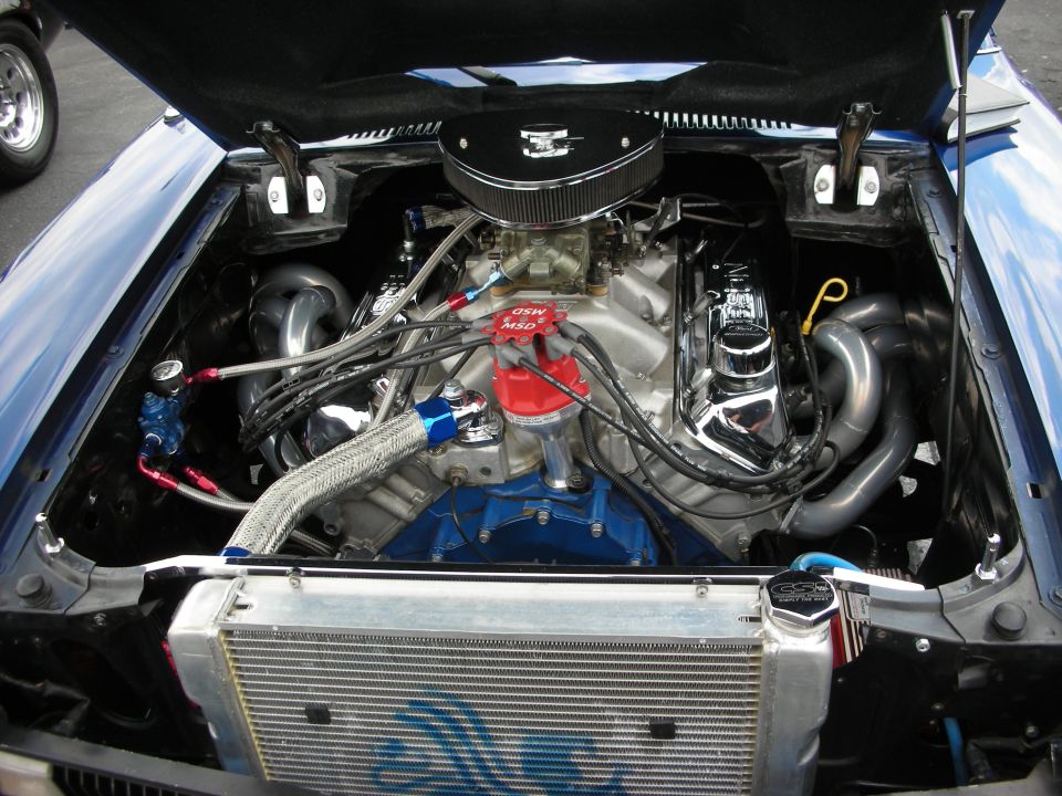 Engine bay of a blue car showing a V8 engine with chrome valve covers and headers, MSD distributor, and aftermarket radiator