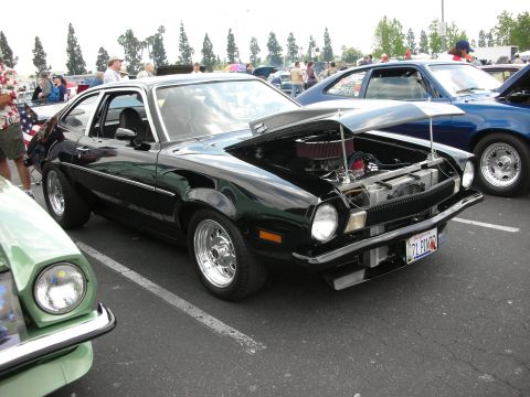 1992 Ford Crown Victoria - A black 1971 Ford Pinto coupe is displayed with its hood open, revealing the engine, at an outdoor car show.