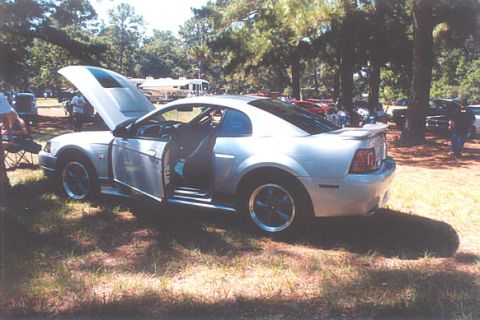 2002 Ford Crown Victoria - A silver coupe, possibly a Ford Mustang, is parked outdoors with its hood and driver's door open.